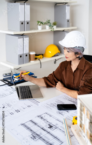 Senior female engineer designer or contractor working on drawing plans analyzing structure on laptop computor at construction site office. copy space.