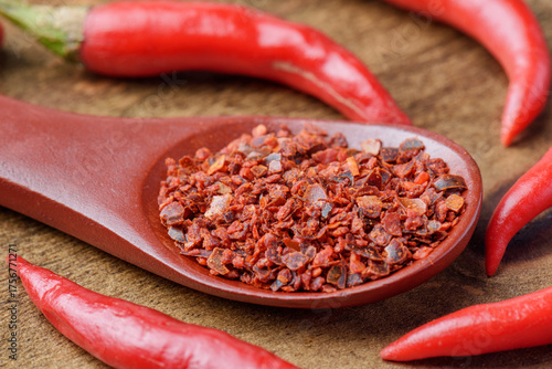Wooden spoon of dried chili pepper flakes among fresh peppers