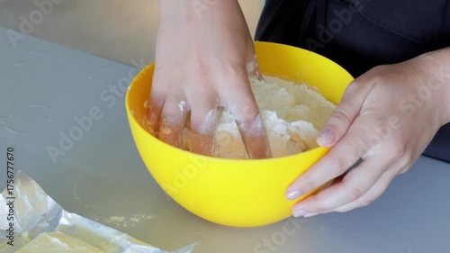Dough preparation process, Hands press and fold powdery ingredients inside yellow vessel, Baker skillfully blends and manipulates flour into dough within vibrant yellow