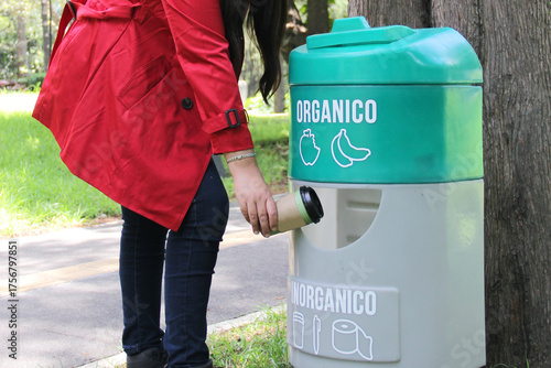Adult Latina woman walking down the street throws coffee cup trash into an organic and inorganic trash can to protect the environment