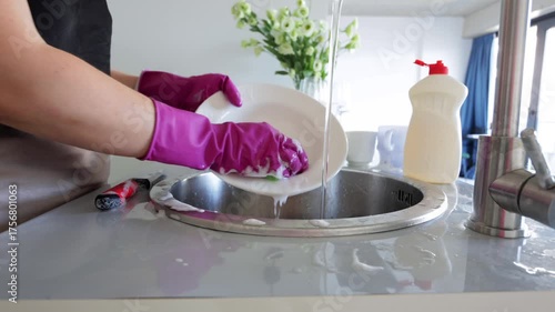 Hands washing dishes with gloves, Female hands scrubbing plates with foam soap, Everyday domestic chore of washing dishes using gloves and cleaning agents in kitchen