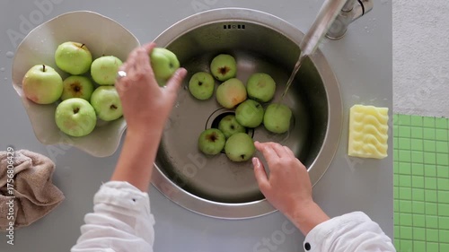 Washing produce before cooking, Preparing fruit by rinsing under tap stream, Thoroughly rinsing fresh green apples beneath flowing water prior to cooking or snacking