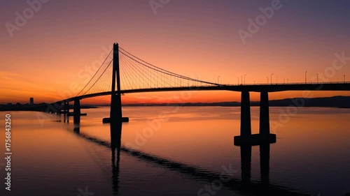 Silhouette of a cable stayed bridge at sunset reflecting in water