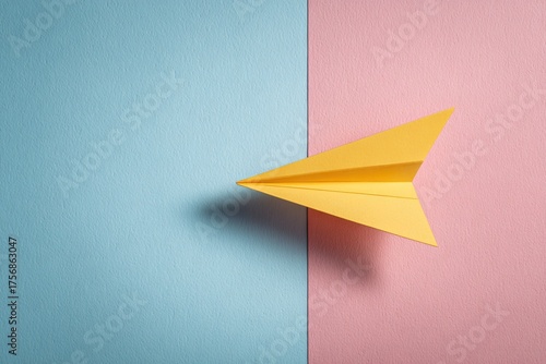A vibrant yellow paper airplane poised between blue and pink paper, creating a colorful, minimalist scene