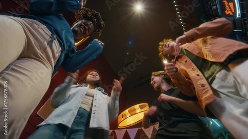 Low angle shot of group of smiling young people dancing cheerfully, celebrating birthday in dimly lit bar