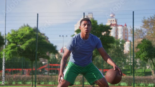 Portrait of concentrated motivated sporty fit black man basketball player practicing streetball game, performing ball dribbles skills during sports training on outdoor court.