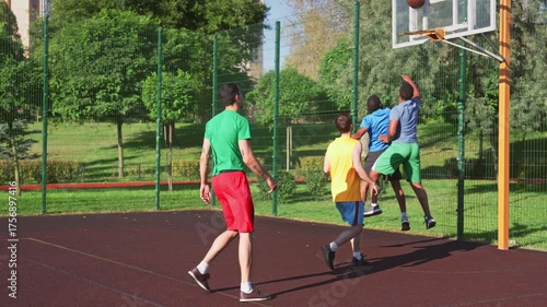 Active sporty fit African American man basketball player driving to the hoop , missing field goal, making offensive rebound and scoring points while multiracial athletes playing streetball on court.