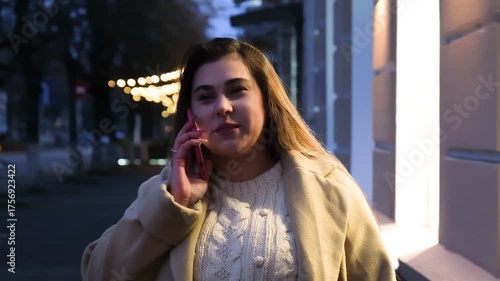 young woman standing outdoors on night neon street cafe illuminated for new year, talking on the phone