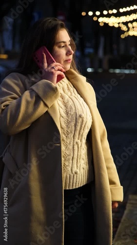young woman standing outdoors on night neon street cafe illuminated for new year, talking on the phone
