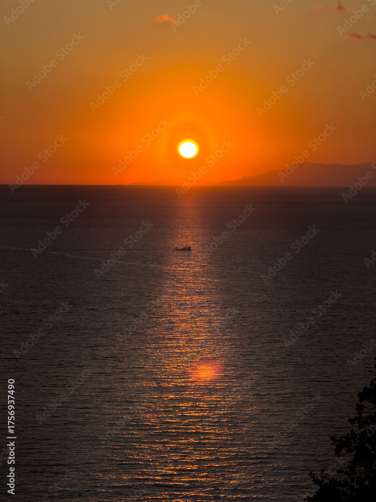 Naklejka premium Golden sunset reflecting on sea with a small boat in reflection