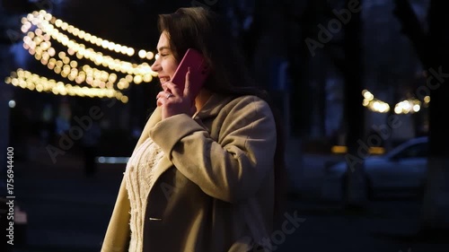 young woman standing outdoors on night neon street cafe illuminated for new year, talking on the phone