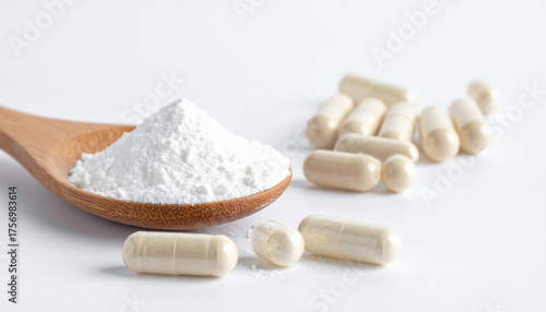 White powder in wooden spoon beside light colored capsules supplements health