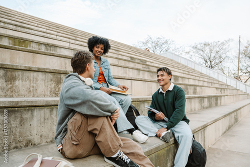 A group of three students sit on the bleachers while two of them smile and listen to the other