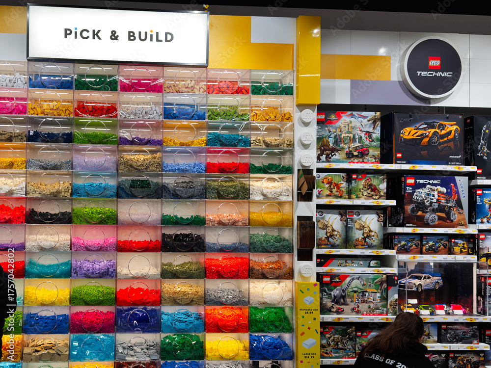 Fototapeta premium Colorful Lego bricks display at a toy store with shoppers and a family