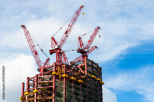 Low-angle view of cranes and steel structures of building construction with a blue sky background in Taiwan.