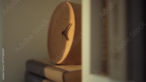 A wooden clock is positioned next to neatly stacked books on a shelf, depicting a tranquil indoor environment that suggests a love for reading and timekeeping