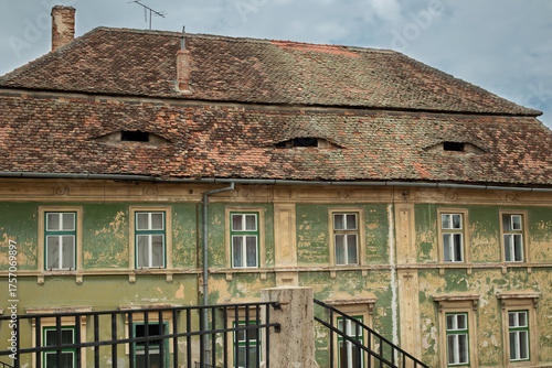 An old historic building with peeling facade, wooden windows, and old roof tiles. Romania, Sibiu.
