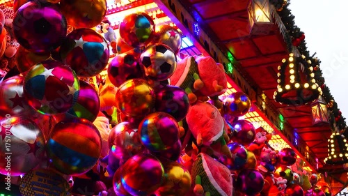 Colorful display of toys and balloons at a fairground in festive lights during the evening. Christmas market