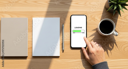 A person is using a smartphone on a wooden desk with a notebook, pen, and cup of coffee. The scene is shot from overhead in a flat lay style. The phone is showing a calling screen.
