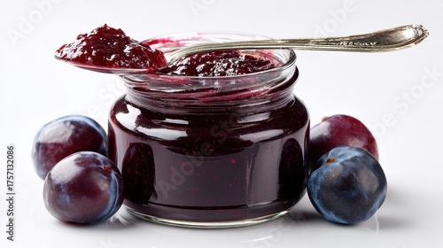 Homemade plum jam in glass jar with fresh blue plums and spoon, showcasing rich dark purple preserve for breakfast and baking recipes