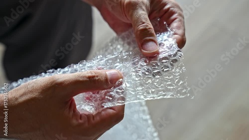 Close up video of hands popping air bubbles on plastic bubble wrap. Concept of relaxation, stress relief, and sensory satisfaction