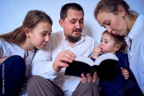 a family with toddler and teenager reading the Bible during Christmas celebration