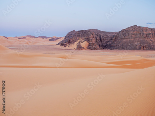 Landscape of the Red Tadrart with dunes and rock formations at sunrise in the Sahara Desert, Algeria.