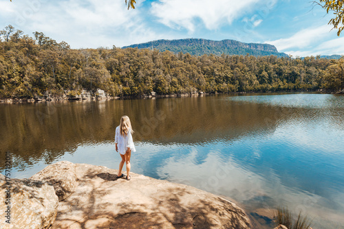 Woman in flowy white shirt stands on rock by river