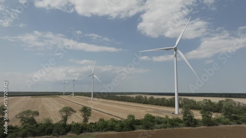 Aerial view of a working wind turbines against the backdrop of agricultural fields.
