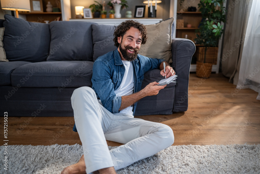 Fototapeta premium Man writing notes in notebook smiling at home
