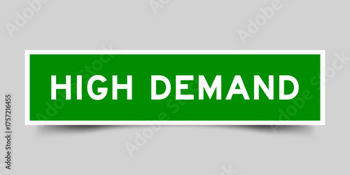 Green color square shape sticker label with word high demand on gray background