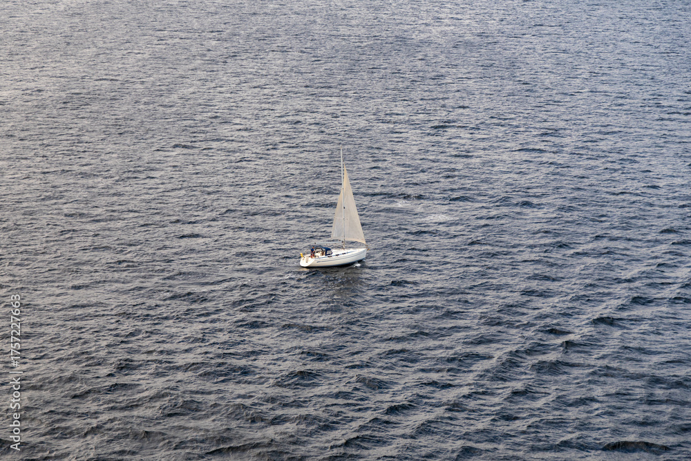Fototapeta premium A lone sailboat drifts on a vast ocean, captured from above in soft light.