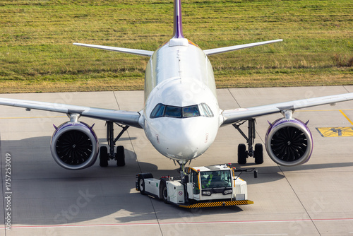 Modern regional jet aircraft towed by ground vehicle on airport taxiway tarmac under sunlight. Engine cockpit clearly visible crew performs technical operations before next scheduled flight airport