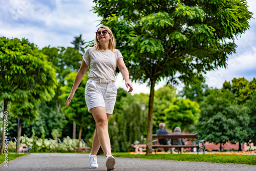 Beautiful middle aged woman walking in city park on summer day. Front view	