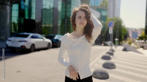 Young woman with curly hair holding head in pain on city street portrait