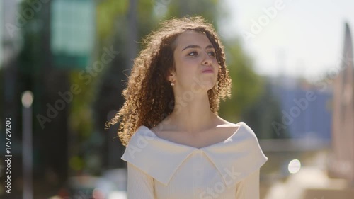 Confident young woman walking on sunny urban street in casual white blouse