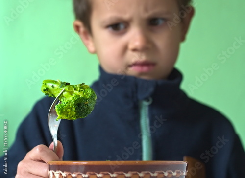 A young boy looks down at a floret of broccoli on a fork with a clear expression of dislike or disgust. This is a classic, humorous, and relatable clip about picky eaters and the struggle to get kids 