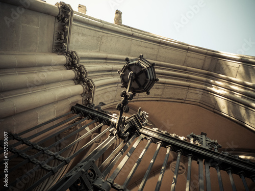 Vintage iron gate and gothic arch under soft light, viewed from below with architectural elegance. Historic iron gate and ornate lamp under stone archway, captured from below with dramatic view.