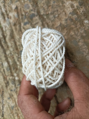 A white yarn ball held in a human hand with a natural background, showing fiber texture and soft details under warm natural light.