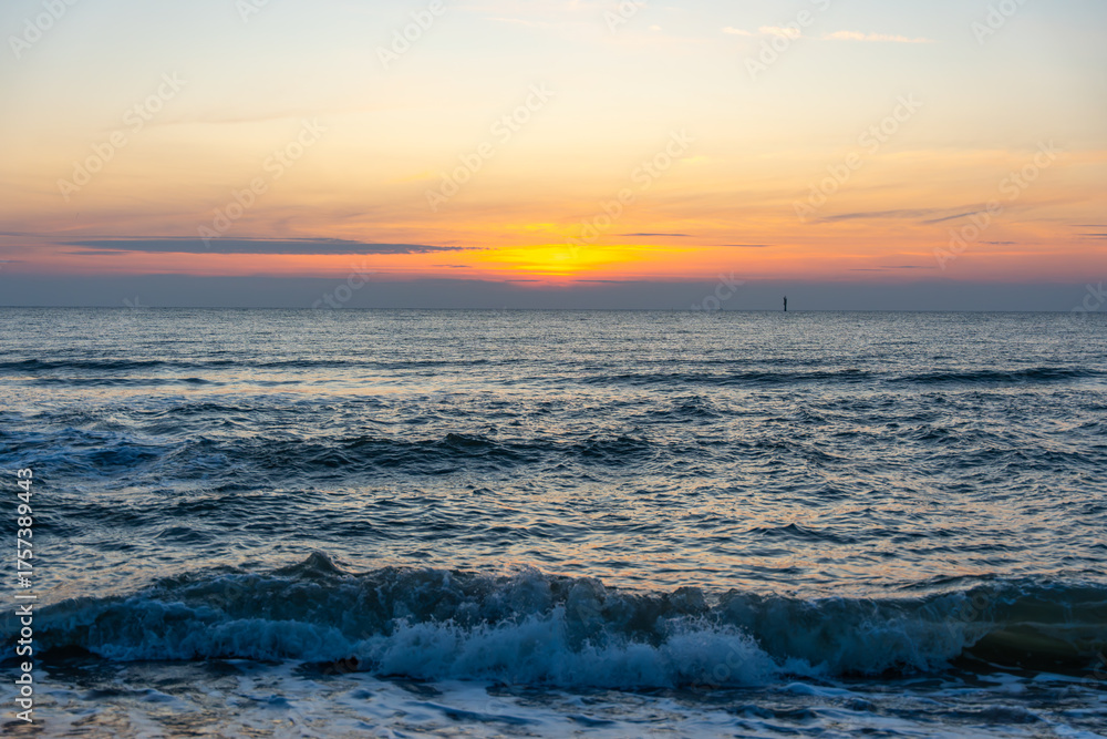Obraz premium Soft evening colors glow above the calm sea at sunset. Gentle waves shimmer under orange and blue skies.