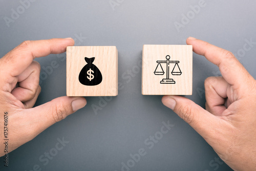 Two wooden blocks held by hands showing a money bag and justice scale representing the decision between profit and ethics in business and moral judgment