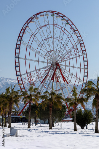Snowy waterfront promenade with ferris wheel and mountains in coastal city