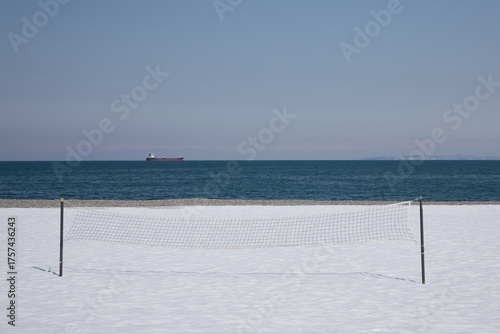 Volleyball net on snow covered beach with cargo ship on sea horizon