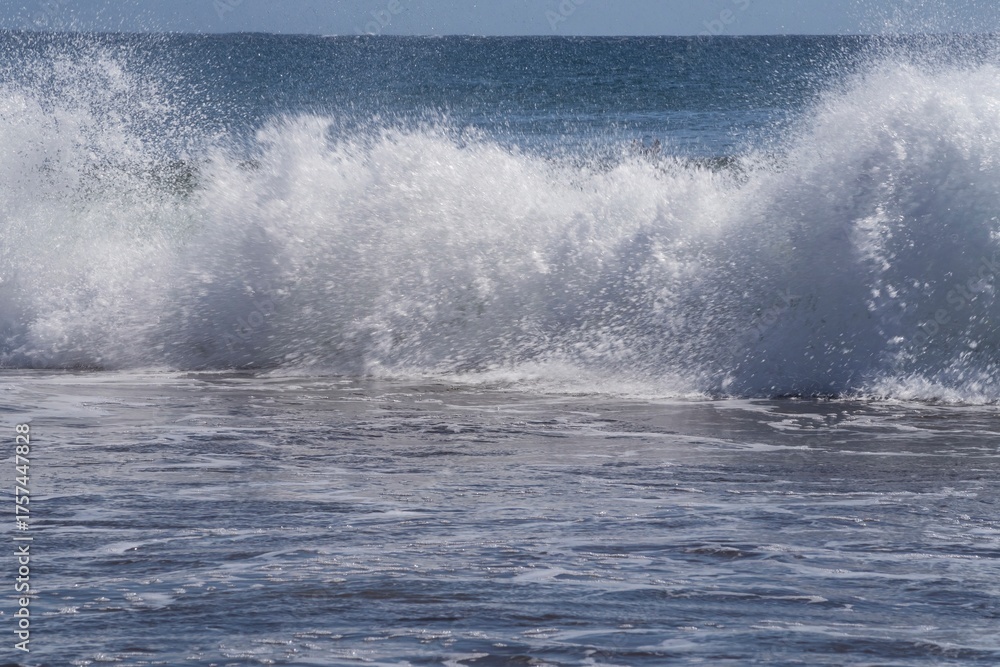 Fototapeta premium Dynamic ocean wave with foam and spray on the volcanic beach of Tenerife. Beautiful natural seascape showing strength, motion, and contrast of deep blue Atlantic water.