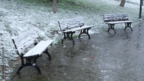 Snowflakes are falling on empty snowy benches in a public park  in slow motion