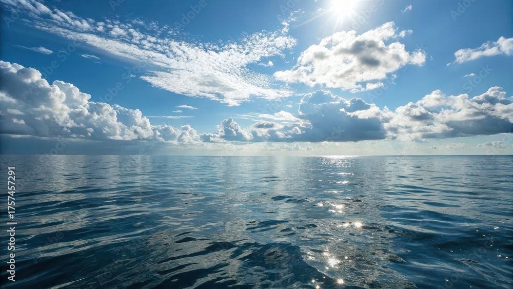 Fototapeta premium A serene ocean view under a bright sky, featuring calm waters reflecting sunlight and scattered clouds.