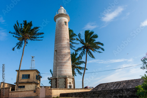 View of a lighthouse standing tall against the azure sky, with palm trees swaying gently in the breeze, in Galle, Southern Province, Sri Lanka.