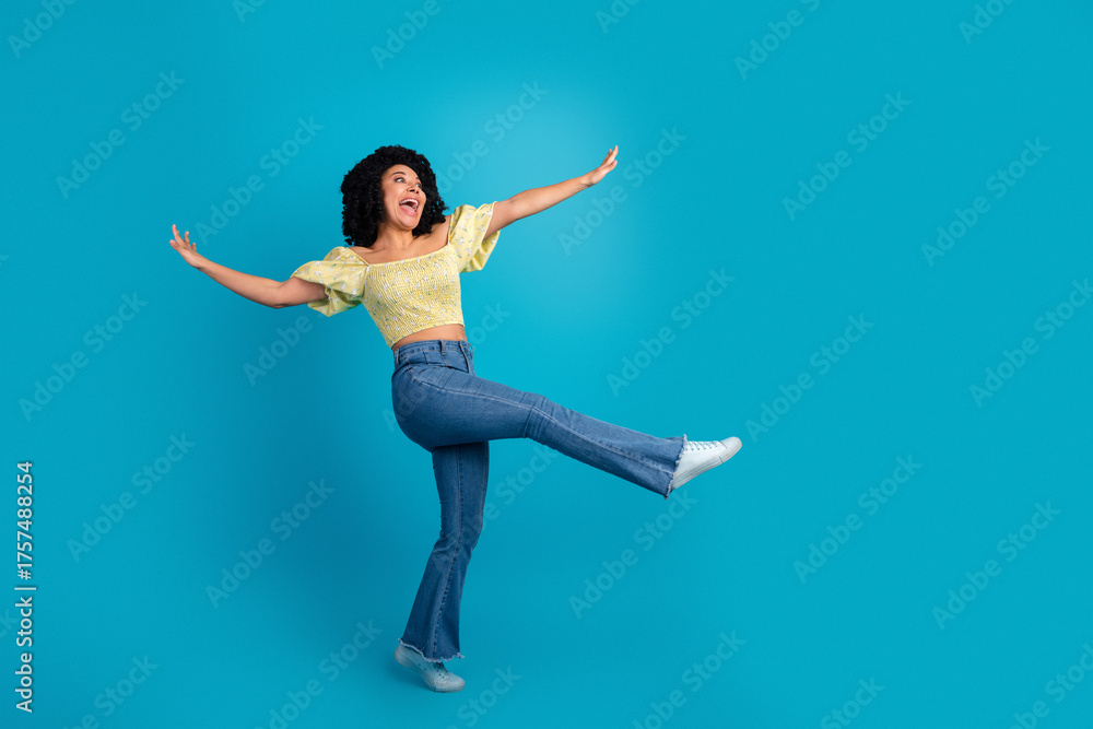 Obraz premium Joyful young woman with curly black hair expressing happiness in casual outfit on a bright blue background