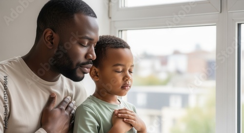 Black father and son praying together with eyes closed. African American family practicing mindfulness and gratitude. Fatherhood and spirituality concept