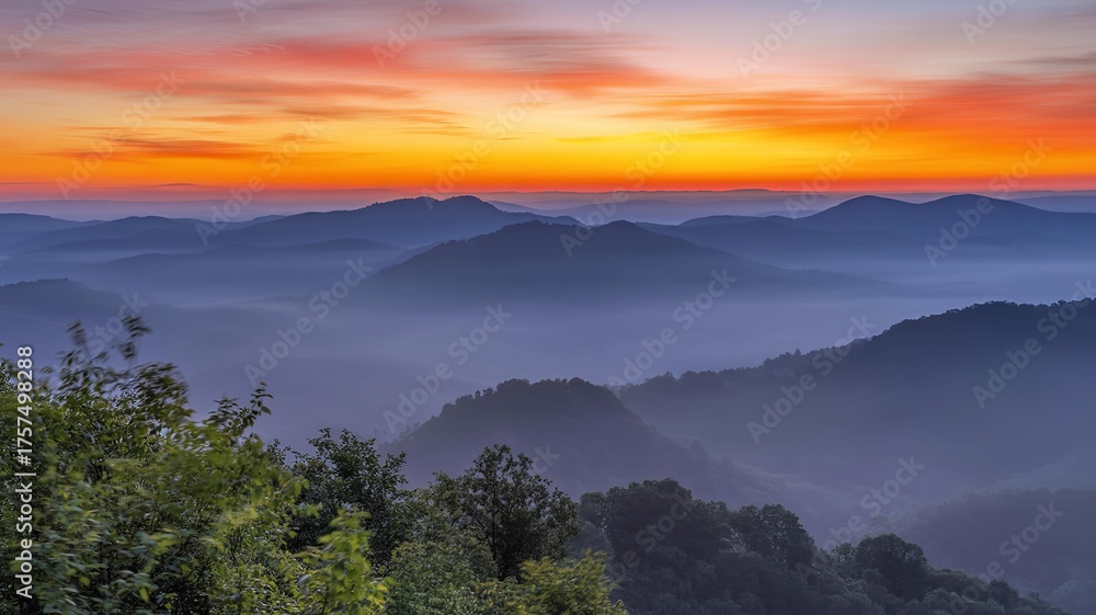 Obraz premium A scenic view of mountains covered in fog with a vibrant orange and pink sunset sky above them all